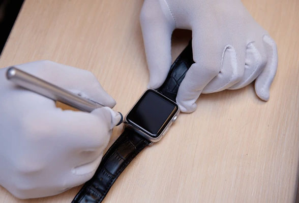 Person wearing gloves adjusting a smartwatch on a wooden surface