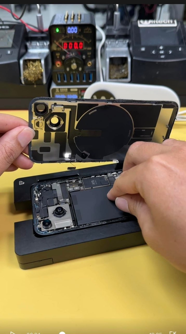 Person repairing a smartphone with its back cover removed on a yellow surface.