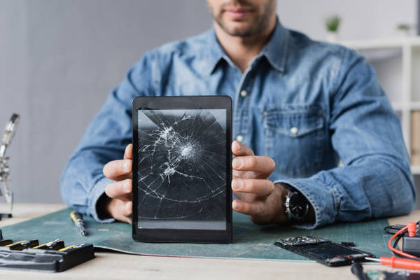 Person holding a tablet with a broken screen in a repair setting