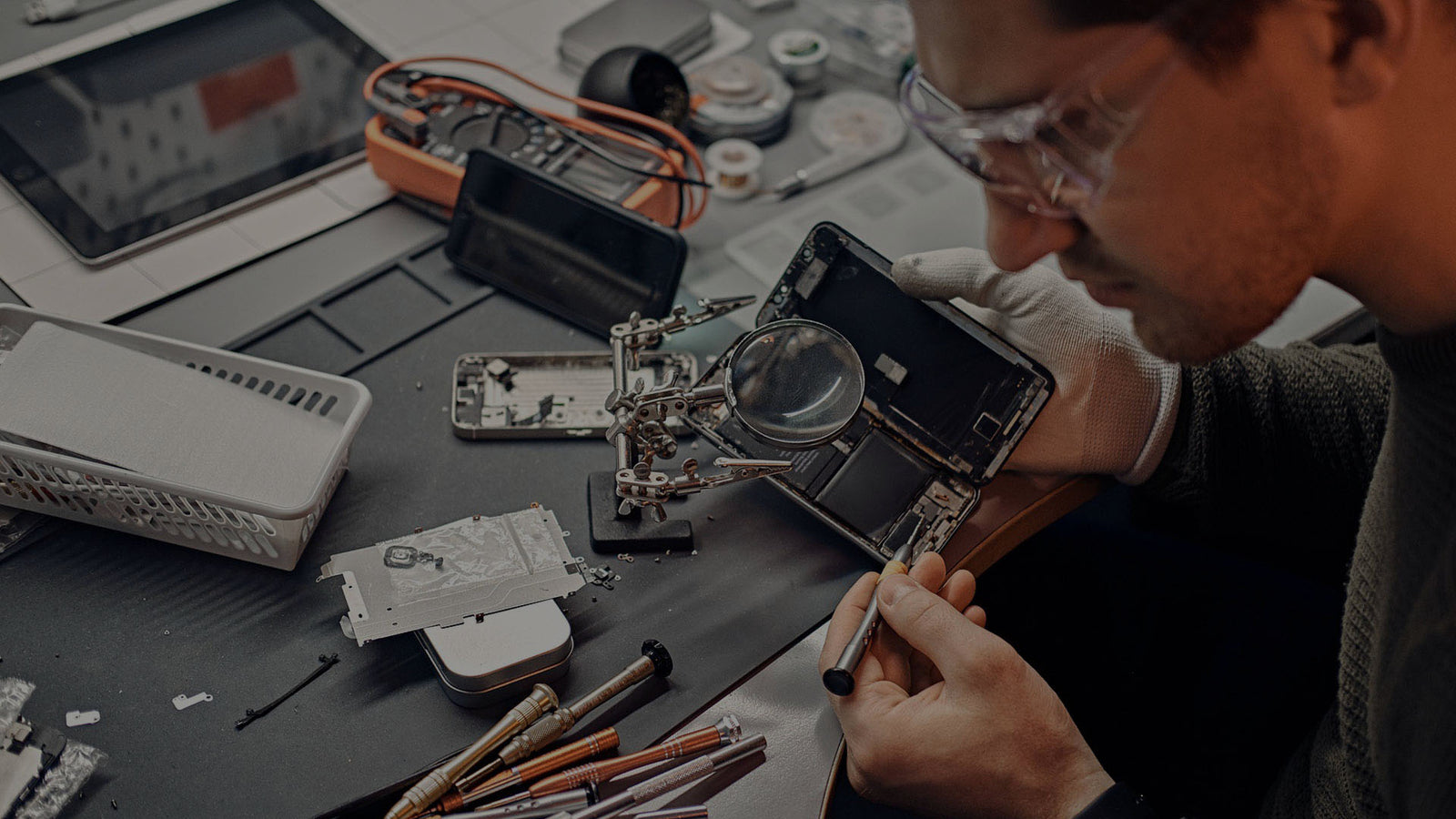 Person working on disassembling a smartphone with tools and parts on a table.
